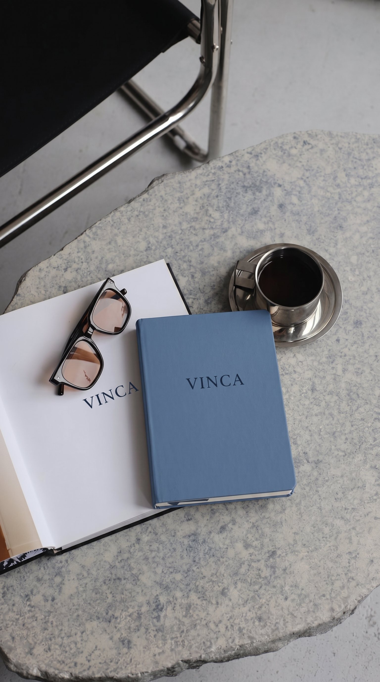 Glasses and a VINCA notebook beside a cup of coffee on a stone table