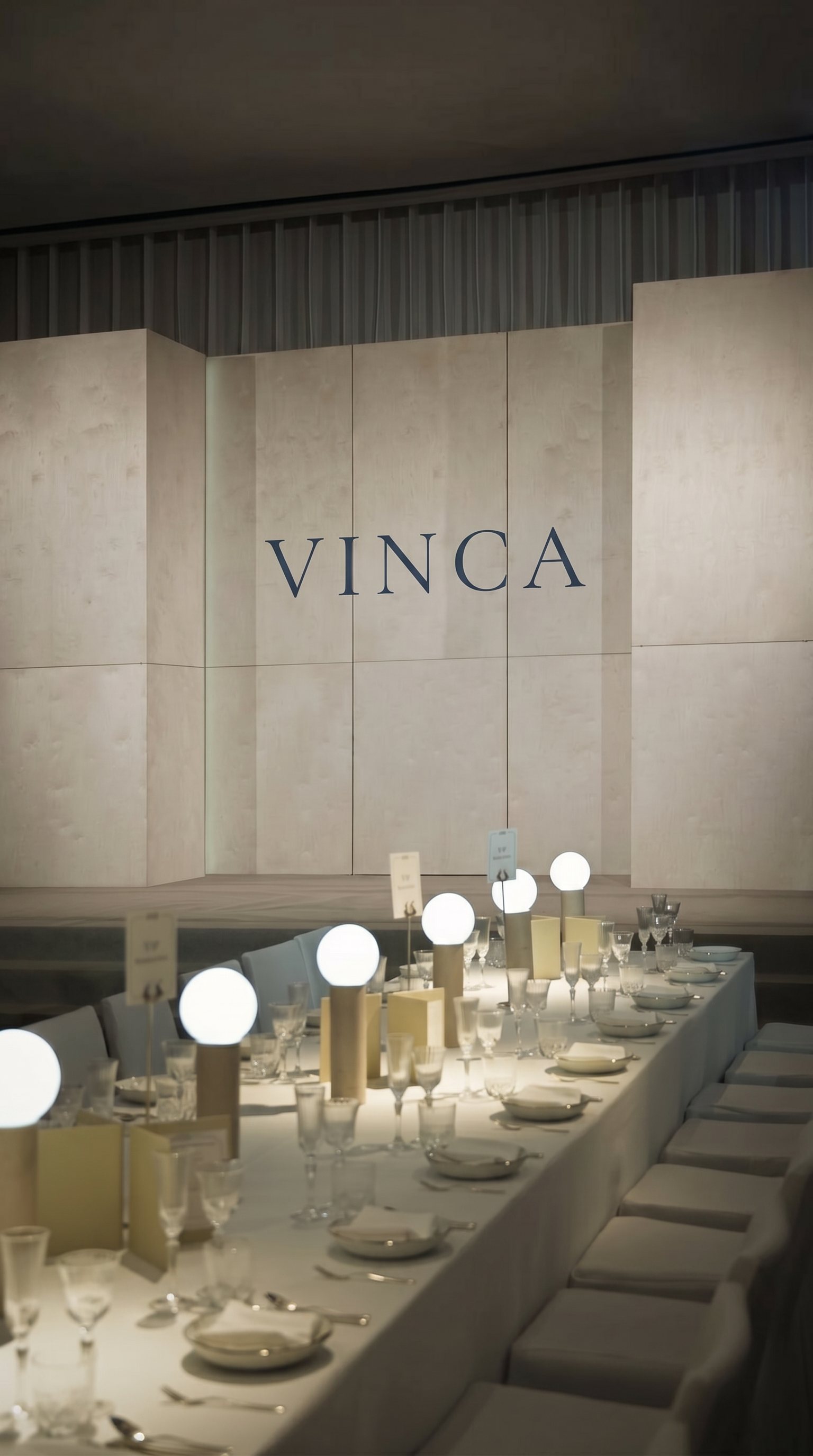 A long formal dinner table set beneath a wall reading VINCA