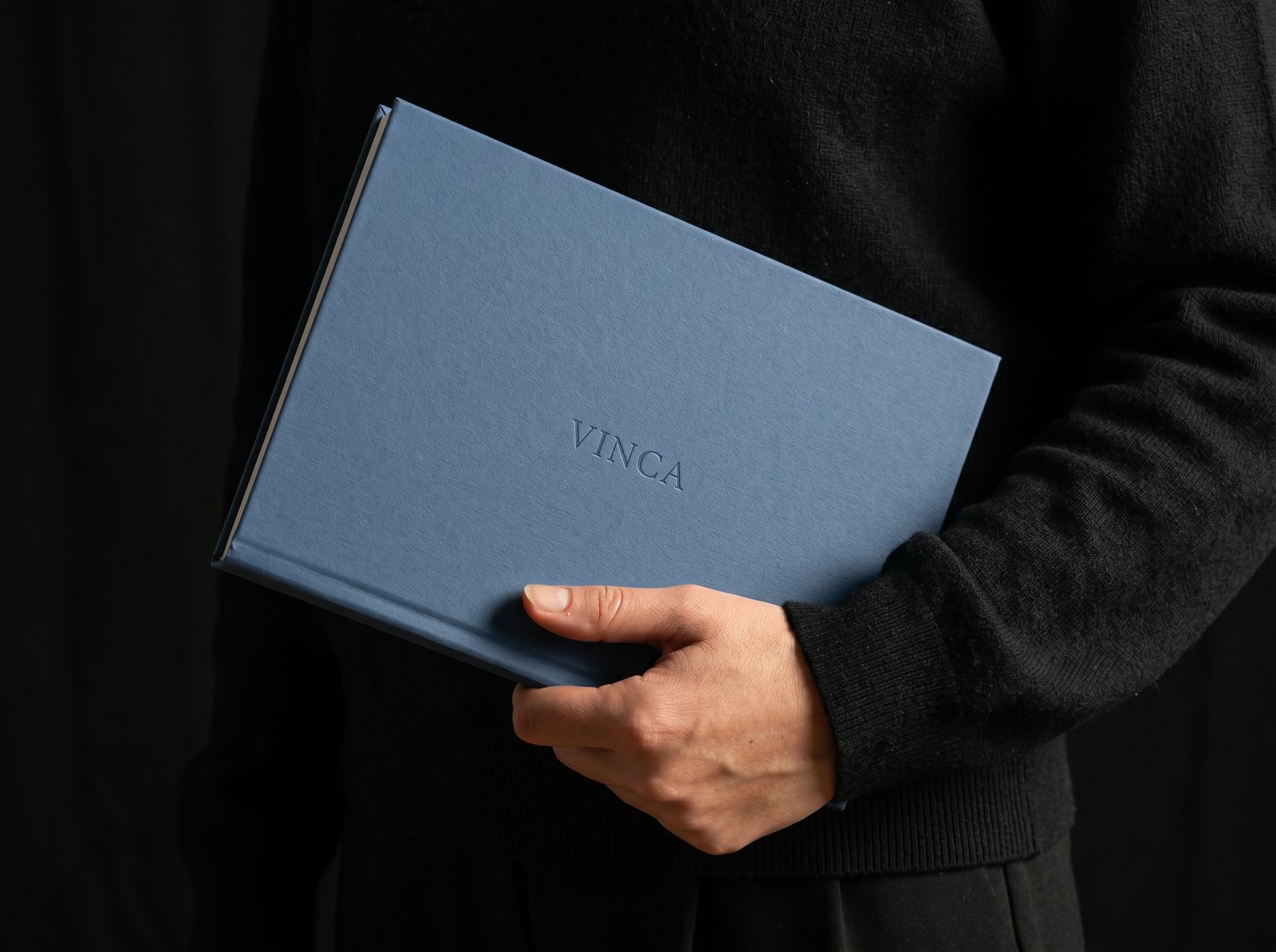 A hand holding a blue VINCA-embossed notebook